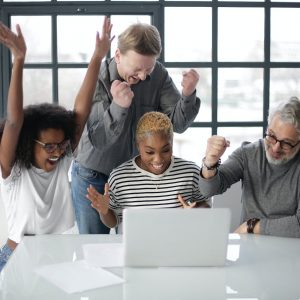 excited multiracial colleagues enjoying triumph together in front of laptop in office